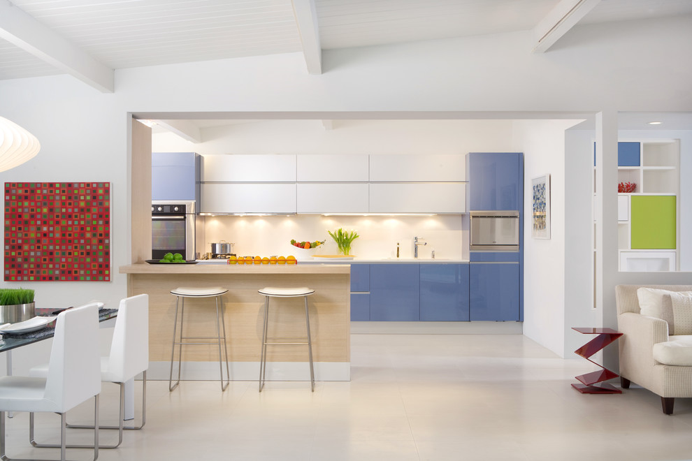 Design ideas for a contemporary galley open plan kitchen in Los Angeles with flat-panel cabinets, blue cabinets, a double-bowl sink, quartz benchtops, white splashback, glass tile splashback, stainless steel appliances, porcelain floors, with island, beige floor and white benchtop.