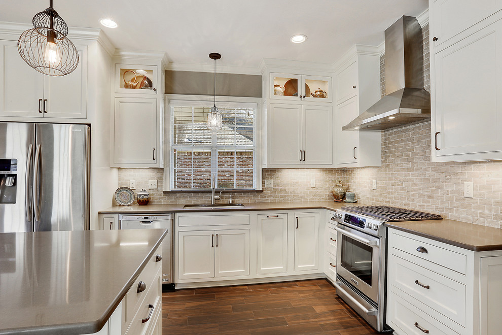 Open concept kitchen - mid-sized transitional l-shaped medium tone wood floor open concept kitchen idea in New Orleans with an undermount sink, recessed-panel cabinets, white cabinets, quartz countertops, beige backsplash, subway tile backsplash, stainless steel appliances and an island
