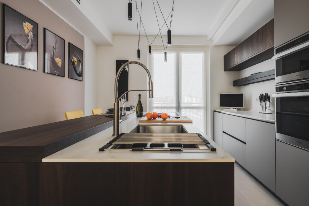 Photo of a mid-sized contemporary galley separate kitchen in Milan with an undermount sink, flat-panel cabinets, grey cabinets, solid surface benchtops, white splashback, stainless steel appliances, porcelain floors, with island, beige floor and white benchtop.