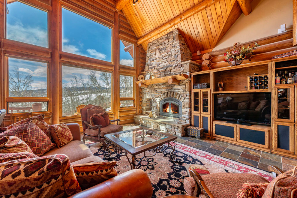Photo of a large country open concept living room in Denver with beige walls, slate floors, a standard fireplace, a stone fireplace surround, a freestanding tv and multi-coloured floor.