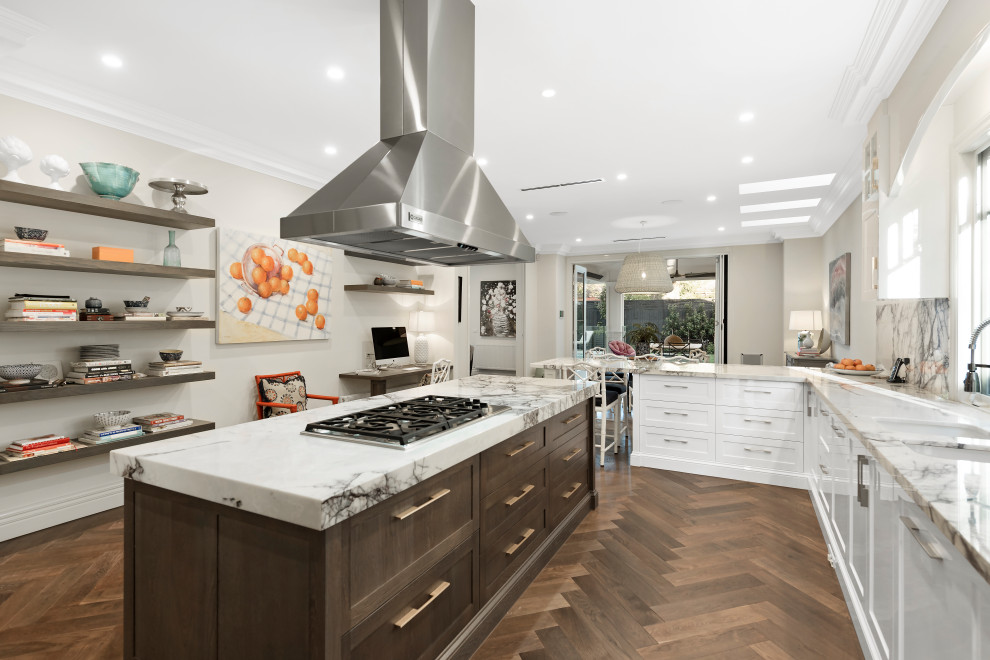 Large transitional l-shaped eat-in kitchen in Melbourne with white cabinets, medium hardwood floors, with island, brown floor, an undermount sink, beaded inset cabinets, marble benchtops, white splashback, marble splashback, stainless steel appliances and white benchtop.