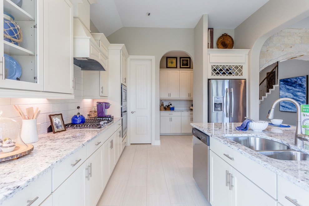 Example of a mid-sized trendy l-shaped ceramic tile and beige floor eat-in kitchen design in Houston with a double-bowl sink, shaker cabinets, white cabinets, granite countertops, white backsplash, subway tile backsplash, stainless steel appliances, an island and gray countertops