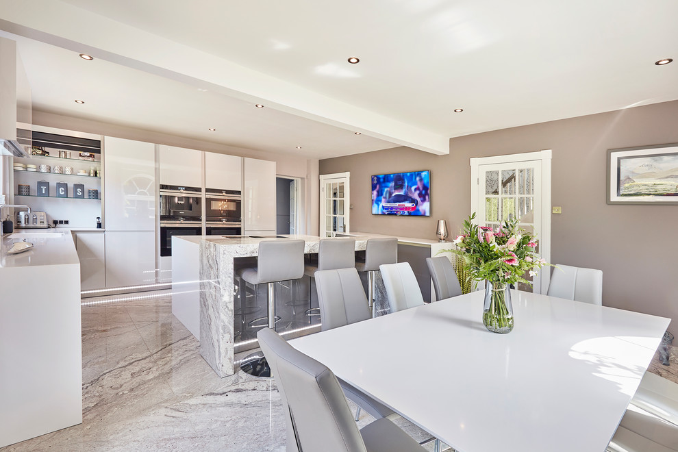 Photo of a mid-sized contemporary l-shaped eat-in kitchen in Other with an integrated sink, flat-panel cabinets, white cabinets, quartzite benchtops, white splashback, granite splashback, black appliances, marble floors, multiple islands, beige floor, white benchtop and coffered.