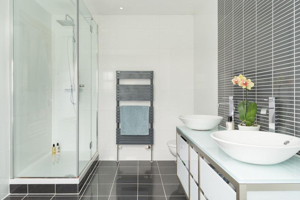 Mid-sized modern master bathroom in London with glass-front cabinets, a corner shower, a one-piece toilet, stone slab, white walls, terra-cotta floors, a trough sink and glass benchtops.