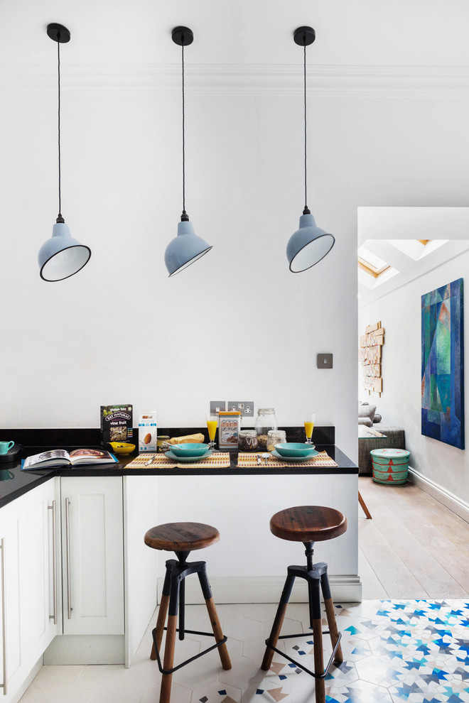 Photo of a mid-sized eclectic galley open plan kitchen in London with an integrated sink, shaker cabinets, white cabinets, granite benchtops, white splashback, glass sheet splashback, stainless steel appliances, porcelain floors and no island.