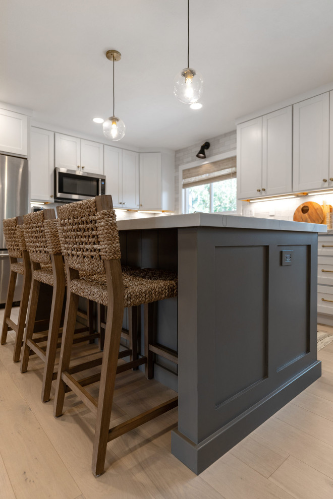 Mid-sized contemporary l-shaped eat-in kitchen in San Francisco with an undermount sink, shaker cabinets, white cabinets, quartzite benchtops, white splashback, ceramic splashback, stainless steel appliances, light hardwood floors, with island, brown floor and white benchtop.