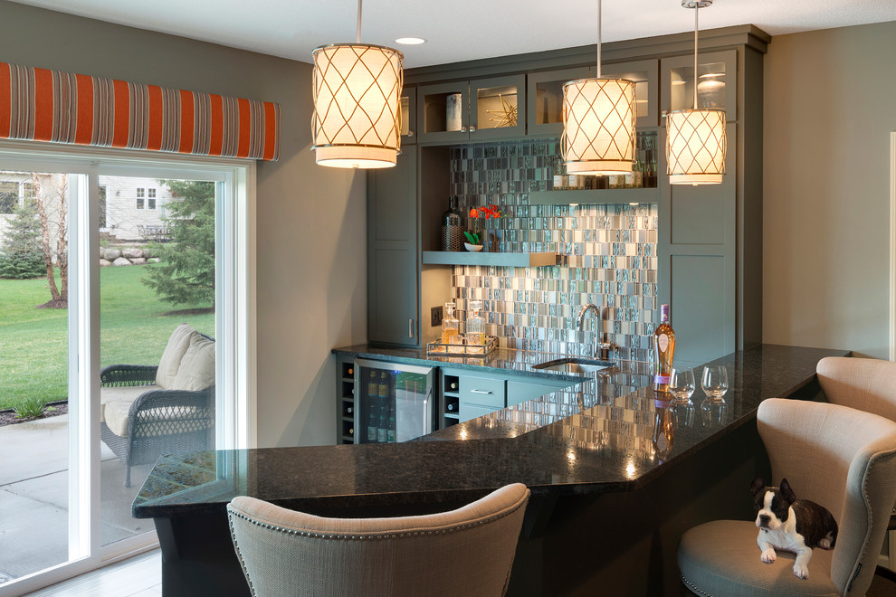 Photo of a mid-sized transitional l-shaped seated home bar in Minneapolis with an integrated sink, shaker cabinets, grey cabinets, granite benchtops, multi-coloured splashback, mosaic tile splashback and porcelain floors.