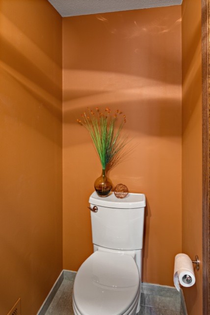 This is an example of a small modern powder room in Minneapolis with an integrated sink, flat-panel cabinets, medium wood cabinets, a two-piece toilet, orange walls, porcelain floors and gray tile.