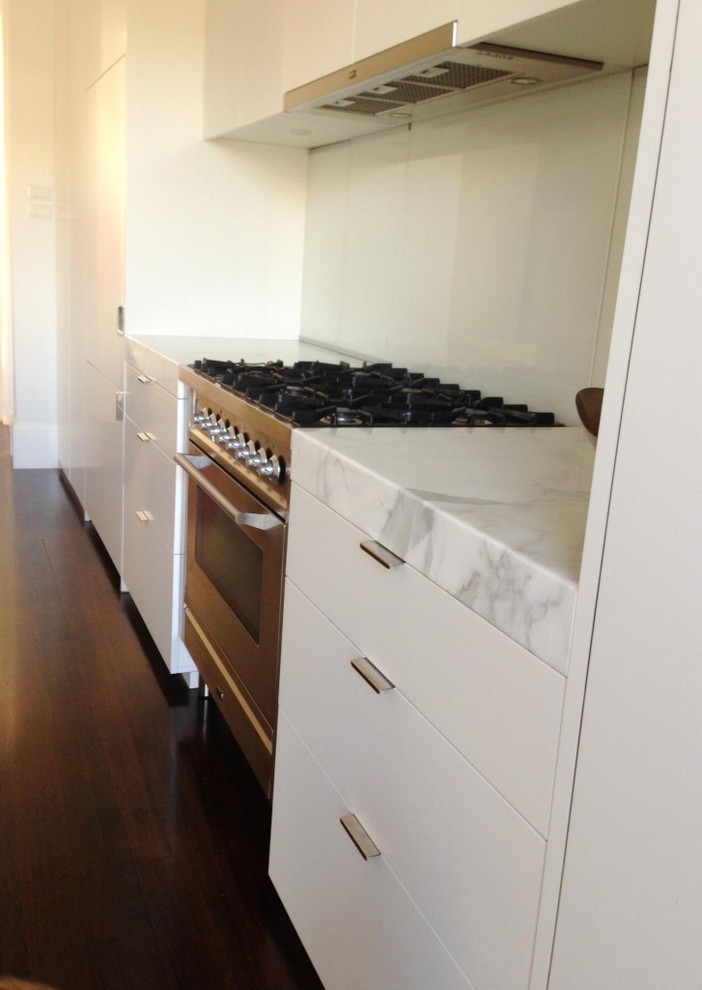 Photo of a contemporary galley kitchen in Melbourne with flat-panel cabinets, white cabinets, marble benchtops, white splashback, glass sheet splashback, stainless steel appliances and with island.