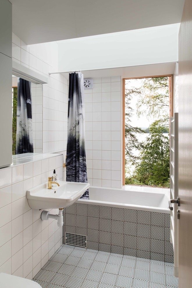 This is an example of a mid-sized contemporary 3/4 bathroom in London with a drop-in tub, a shower/bathtub combo, white tile, porcelain tile, white walls, a wall-mount sink and multi-coloured floor.