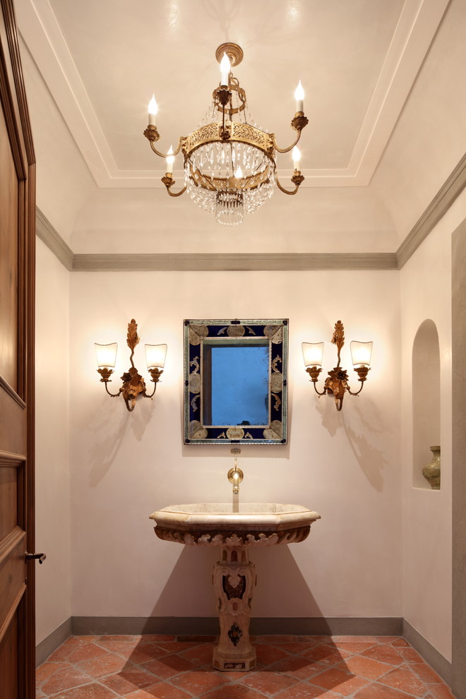 This is an example of a mediterranean powder room in Los Angeles with white walls, terra-cotta floors, a pedestal sink and orange floor.