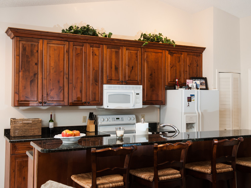 Large transitional galley ceramic tile eat-in kitchen photo in Miami with an undermount sink, dark wood cabinets, granite countertops, white backsplash, white appliances and no island