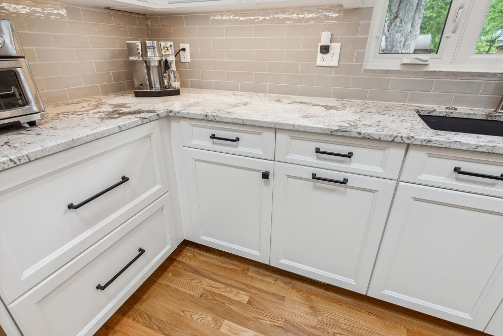 This is an example of a mid-sized traditional l-shaped eat-in kitchen in Columbus with an undermount sink, recessed-panel cabinets, white cabinets, granite benchtops, beige splashback, ceramic splashback, stainless steel appliances, light hardwood floors, with island, brown floor, white benchtop and vaulted.