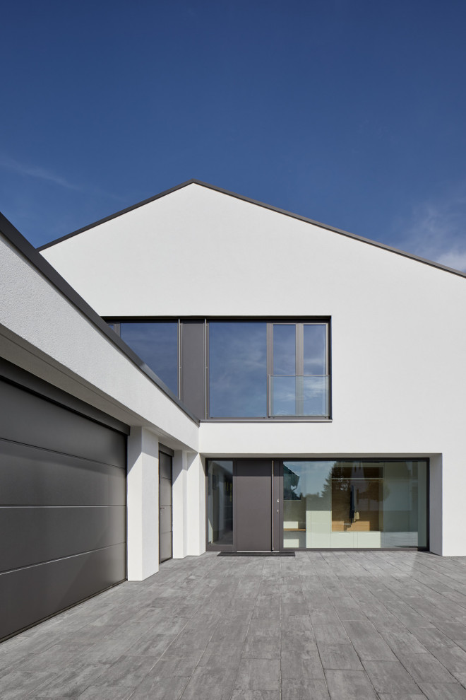 This is an example of a large modern one-storey stucco white house exterior in Cologne with a gable roof and a tile roof.
