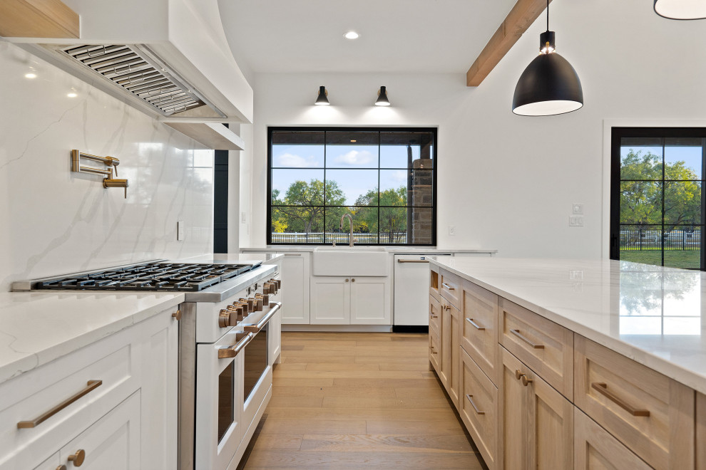 Photo of a country u-shaped open plan kitchen in Austin with a farmhouse sink, shaker cabinets, light wood cabinets, white splashback, marble splashback, white appliances, light hardwood floors, with island, white benchtop and exposed beam.