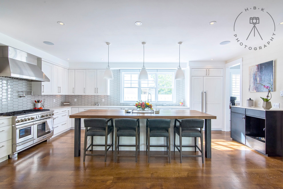Inspiration for a large transitional single-wall medium tone wood floor and brown floor open concept kitchen remodel with an undermount sink, recessed-panel cabinets, white cabinets, wood countertops, white backsplash, ceramic backsplash, stainless steel appliances, an island and brown countertops