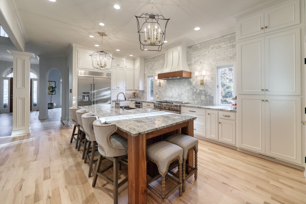 Inspiration for a large eclectic l-shaped eat-in kitchen in Nashville with a farmhouse sink, beaded inset cabinets, white cabinets, granite benchtops, grey splashback, marble splashback, stainless steel appliances, with island and grey benchtop.