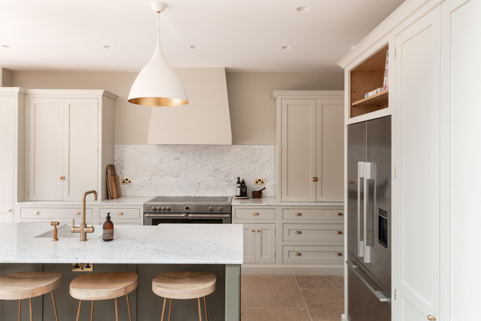 Design ideas for a large traditional single-wall open plan kitchen in London with a built-in sink, shaker cabinets, light wood cabinets, marble worktops, white splashback, marble splashback, black appliances, limestone flooring, an island, beige floors, white worktops, a vaulted ceiling and feature lighting.