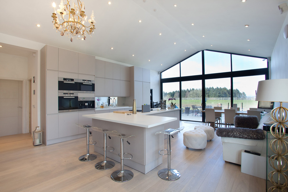 Design ideas for a contemporary eat-in kitchen in London with a single-bowl sink, flat-panel cabinets, beige cabinets, mirror splashback, stainless steel appliances, light hardwood floors and with island.