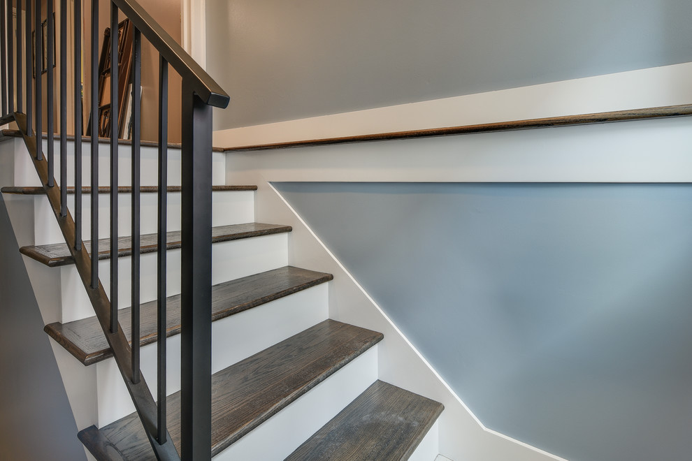 Photo of a large transitional wood u-shaped staircase in Portland with painted wood risers and metal railing.