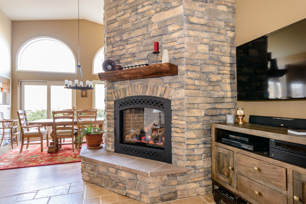 Large country open concept family room in Denver with beige walls, limestone floors, a standard fireplace, a stone fireplace surround, a wall-mounted tv and beige floor.