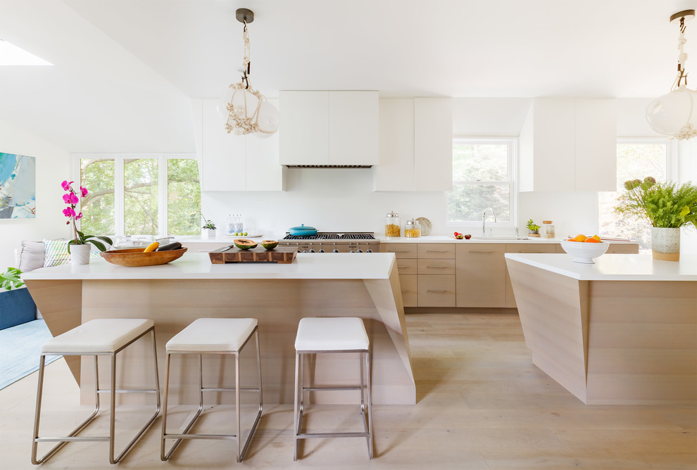 Inspiration for a contemporary open plan kitchen in Boston with an undermount sink, flat-panel cabinets, white cabinets, white splashback, stainless steel appliances, light hardwood floors, multiple islands, beige floor, white benchtop and solid surface benchtops.