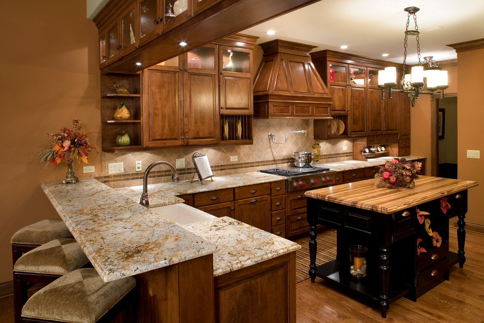 Photo of a large traditional u-shaped eat-in kitchen in Chicago with a farmhouse sink, raised-panel cabinets, distressed cabinets, granite benchtops, beige splashback, ceramic splashback, stainless steel appliances, medium hardwood floors, with island and brown floor.