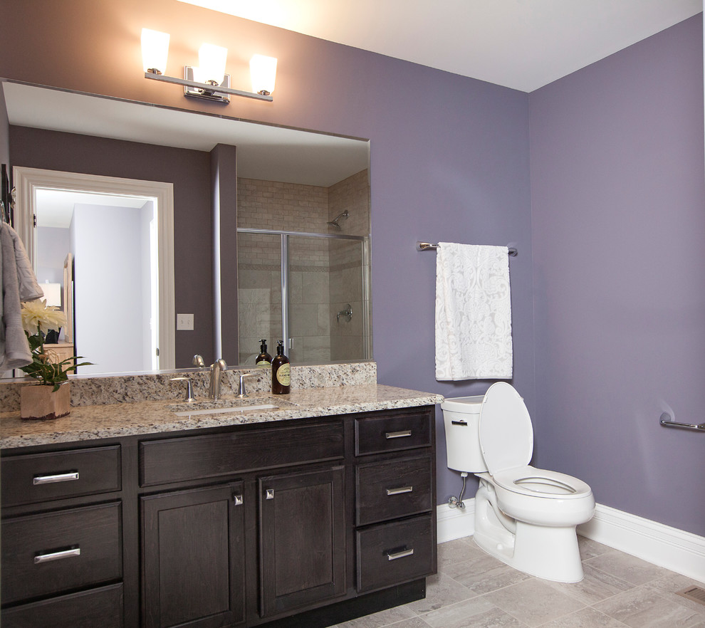Photo of an arts and crafts 3/4 bathroom in Chicago with an undermount sink, recessed-panel cabinets, dark wood cabinets, granite benchtops, an alcove tub, an alcove shower, a two-piece toilet, gray tile, porcelain tile, purple walls and porcelain floors.