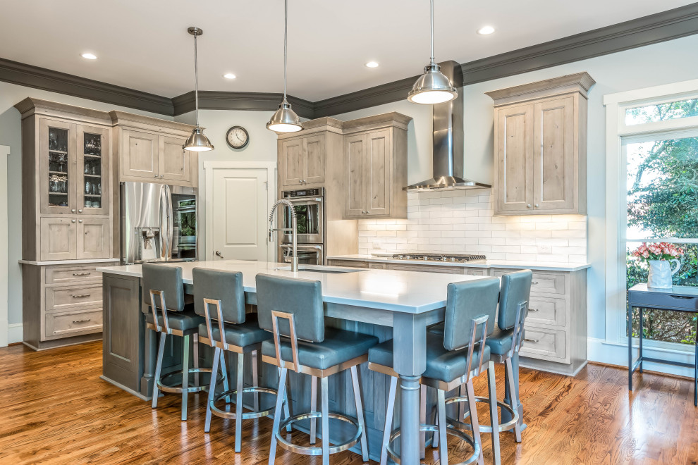 This is an example of a large transitional l-shaped eat-in kitchen in Atlanta with a farmhouse sink, raised-panel cabinets, beige cabinets, white splashback, subway tile splashback, stainless steel appliances, medium hardwood floors, with island, brown floor and white benchtop.