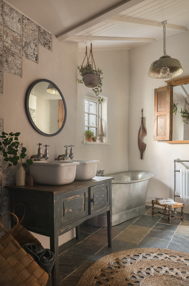 Country bathroom in Cornwall with raised-panel cabinets, distressed cabinets, a freestanding tub, beige walls, a vessel sink, wood benchtops, black floor and black benchtops.