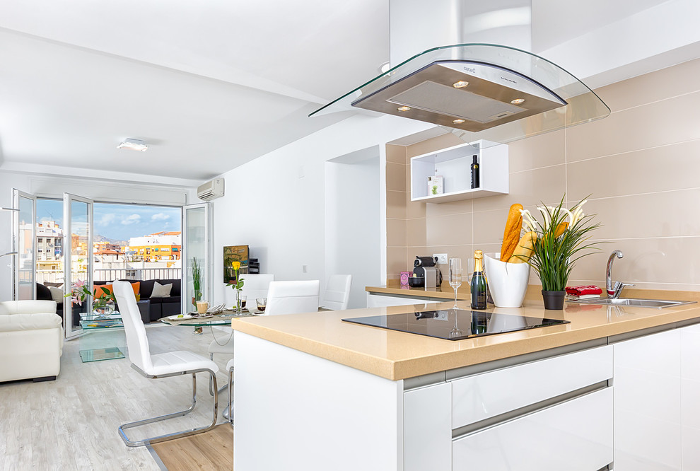 Inspiration for a mid-sized contemporary l-shaped eat-in kitchen in Malaga with flat-panel cabinets, white cabinets, solid surface benchtops, beige splashback, ceramic splashback and a peninsula.