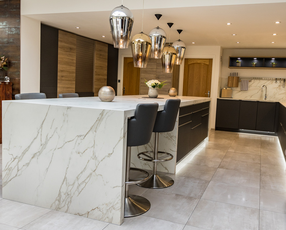 Photo of a large modern l-shaped open plan kitchen in Surrey with an integrated sink, flat-panel cabinets, grey cabinets, solid surface benchtops, white splashback, slate splashback, stainless steel appliances, porcelain floors, with island and grey floor.
