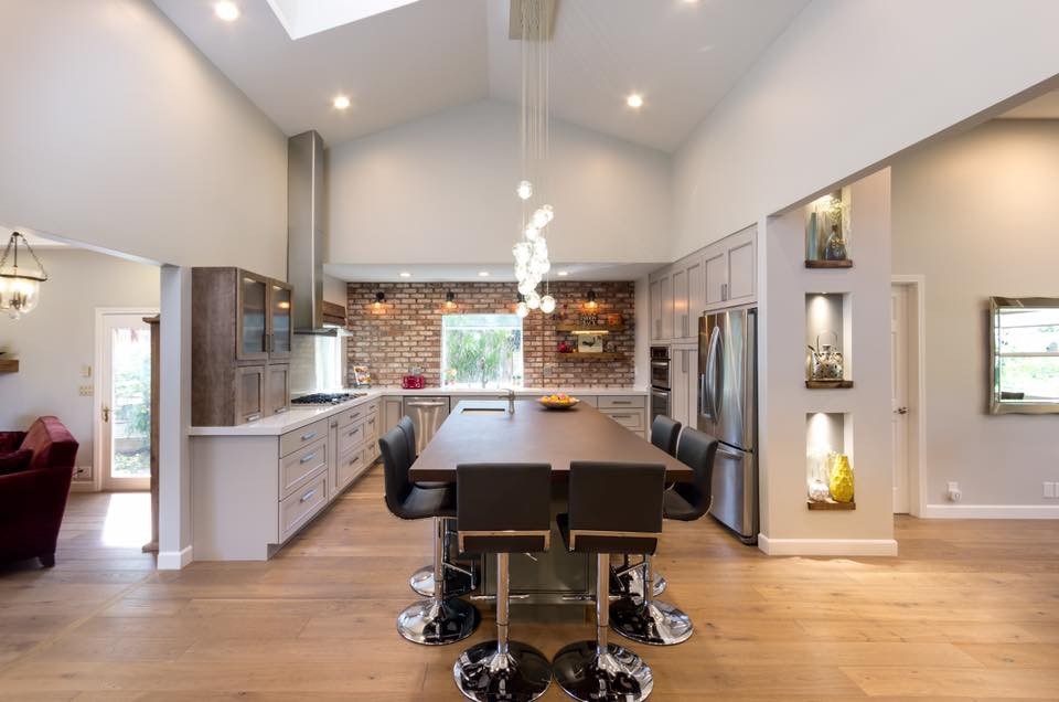 Mid-sized eclectic u-shaped eat-in kitchen in San Francisco with an undermount sink, recessed-panel cabinets, white cabinets, quartz benchtops, brown splashback, brick splashback, stainless steel appliances, light hardwood floors, with island, beige floor and white benchtop.