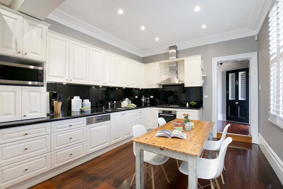 Traditional l-shaped separate kitchen in Newcastle - Maitland with a double-bowl sink, raised-panel cabinets, white cabinets, granite benchtops, black splashback, glass tile splashback, panelled appliances, medium hardwood floors, no island, brown floor and black benchtop.