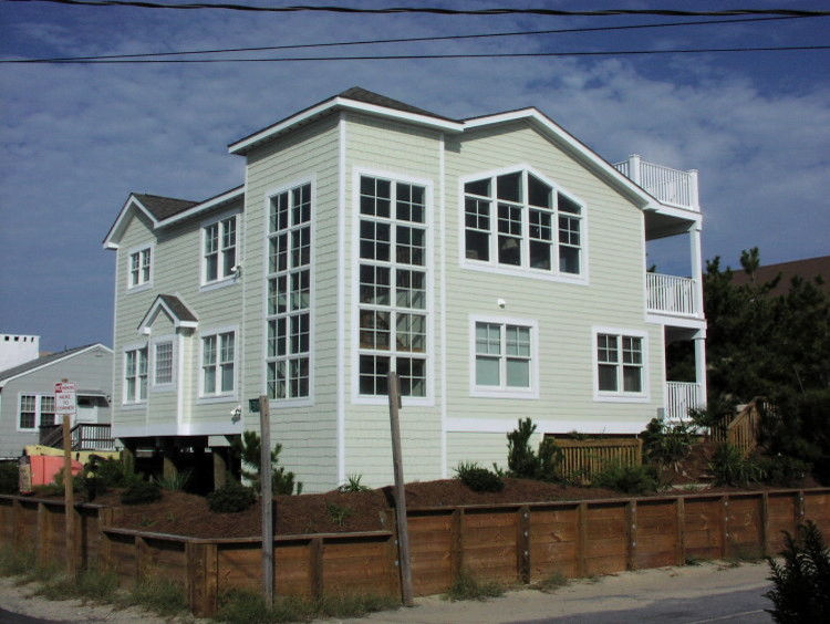This is an example of a large beach style three-storey green house exterior in Other with wood siding, a gable roof and a shingle roof.
