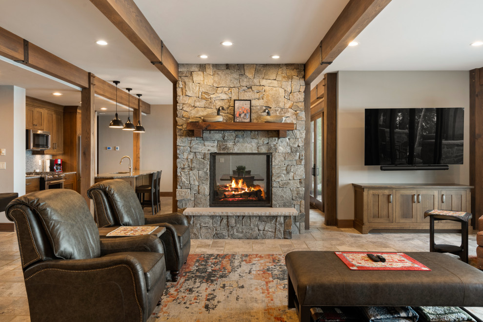 Large open concept living room in Milwaukee with beige walls, travertine floors, a two-sided fireplace, a stone fireplace surround, beige floor and exposed beam.