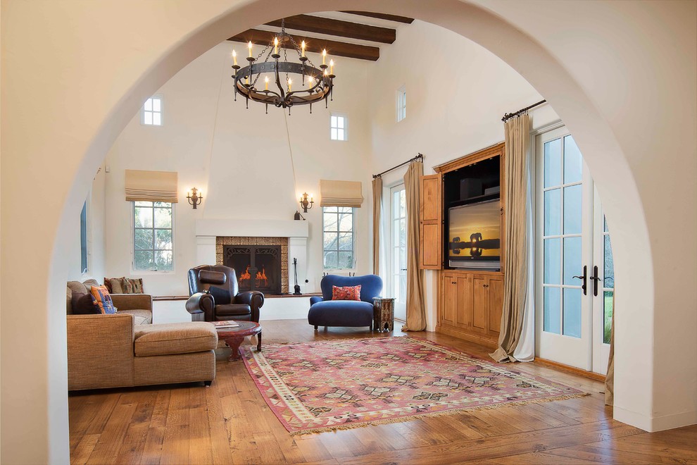 Large mediterranean formal open concept living room in Santa Barbara with white walls, medium hardwood floors, a standard fireplace, a stone fireplace surround and a built-in media wall.
