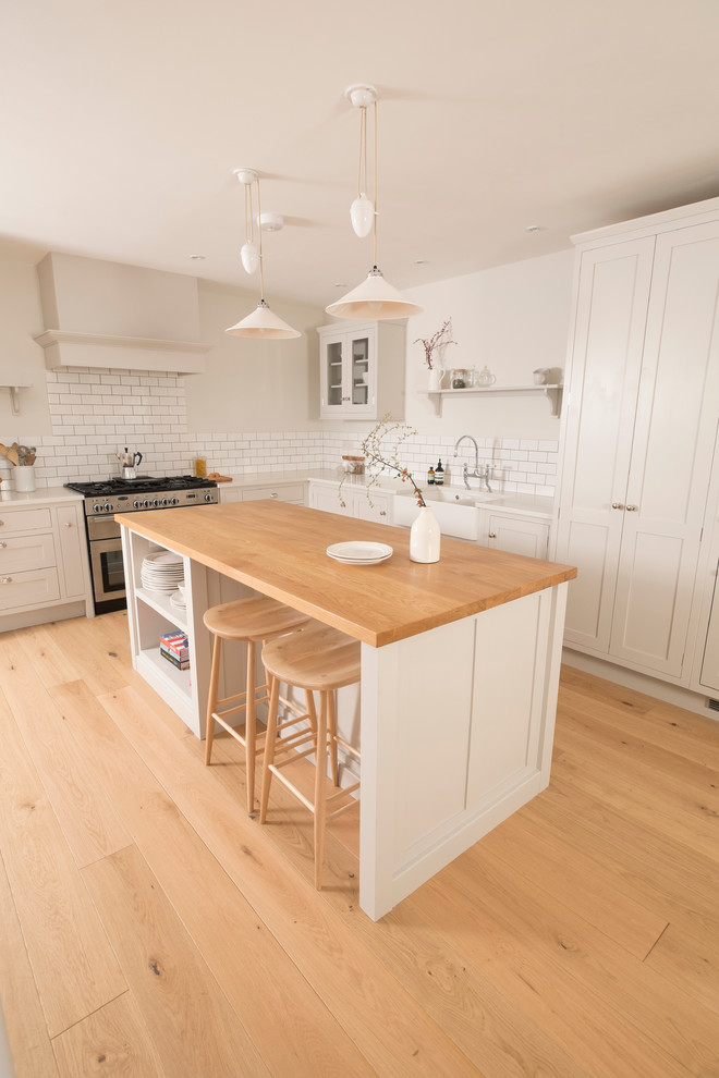 Mid-sized traditional l-shaped open plan kitchen in Cardiff with quartzite benchtops, a farmhouse sink, shaker cabinets, white cabinets, white splashback, subway tile splashback, stainless steel appliances, medium hardwood floors and with island.