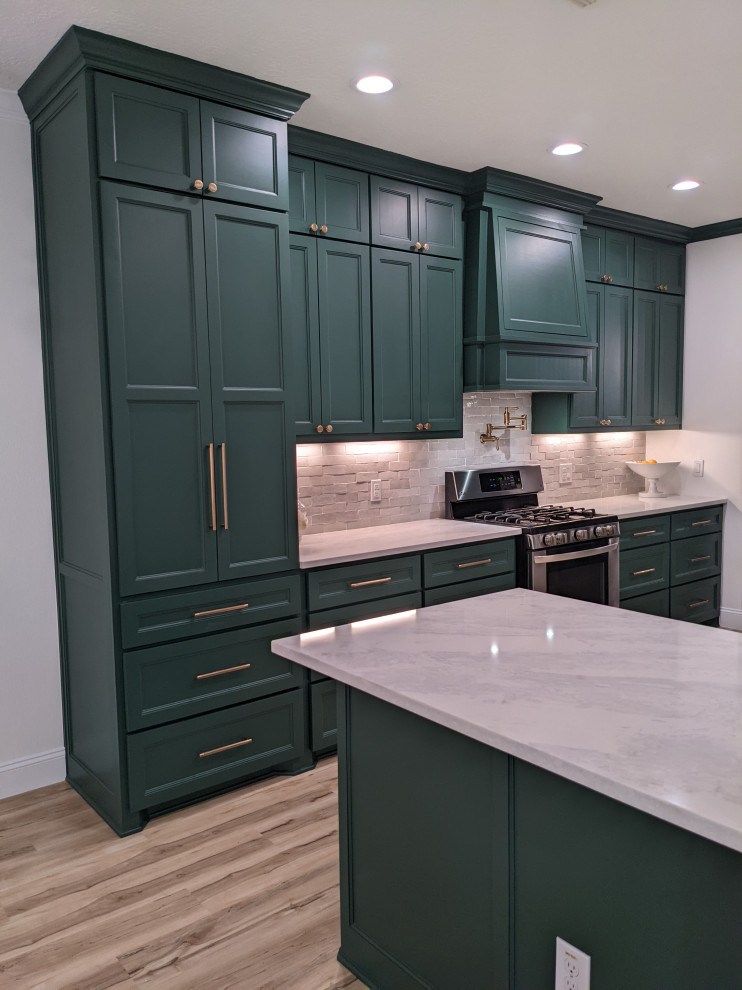 This is an example of a transitional kitchen in Houston with a farmhouse sink, shaker cabinets, green cabinets, quartz benchtops, white splashback, ceramic splashback, stainless steel appliances and white benchtop.