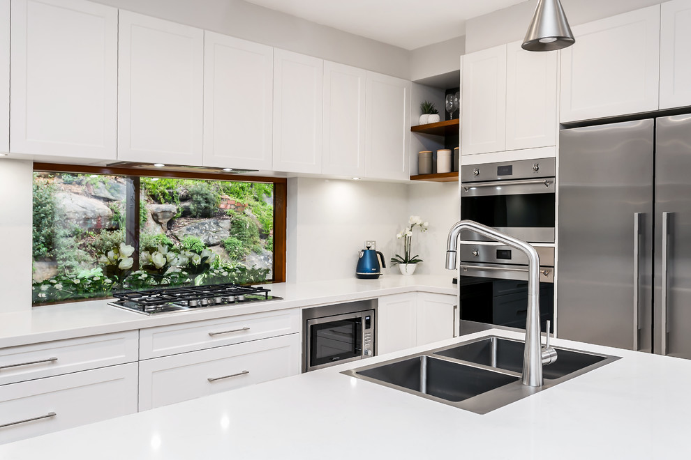 Design ideas for a large contemporary galley eat-in kitchen with a double-bowl sink, shaker cabinets, white cabinets, quartz benchtops, window splashback, stainless steel appliances, light hardwood floors, with island, brown floor and white benchtop.