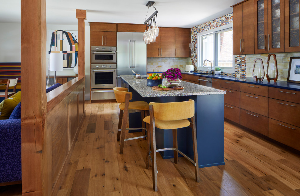This is an example of a midcentury l-shaped open plan kitchen in Denver with flat-panel cabinets, medium wood cabinets, multi-coloured splashback, stainless steel appliances, light hardwood floors, with island and blue benchtop.