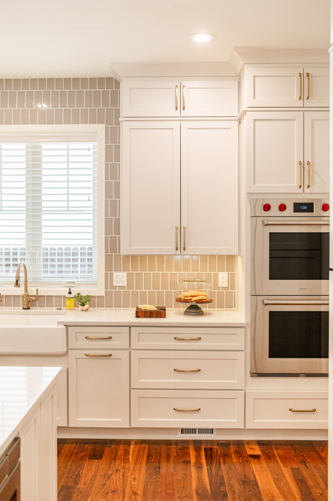 Large transitional l-shaped dark wood floor and brown floor open concept kitchen photo in Denver with a farmhouse sink, shaker cabinets, beige cabinets, quartz countertops, beige backsplash, ceramic backsplash, stainless steel appliances, an island and white countertops
