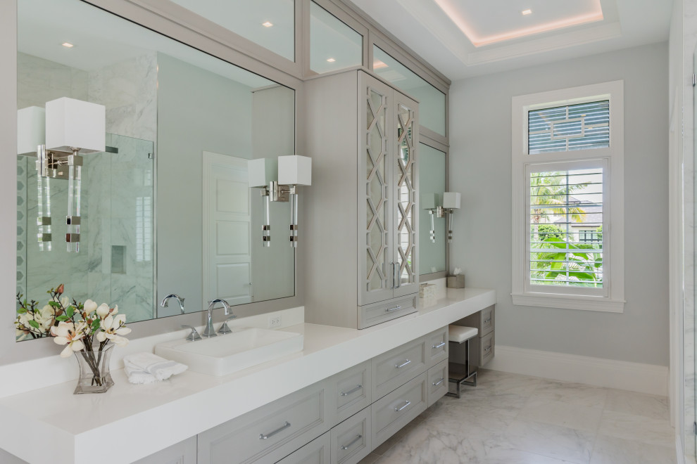 This is an example of a transitional bathroom in Miami with recessed-panel cabinets, grey cabinets, grey walls, a vessel sink, grey floor and white benchtops.