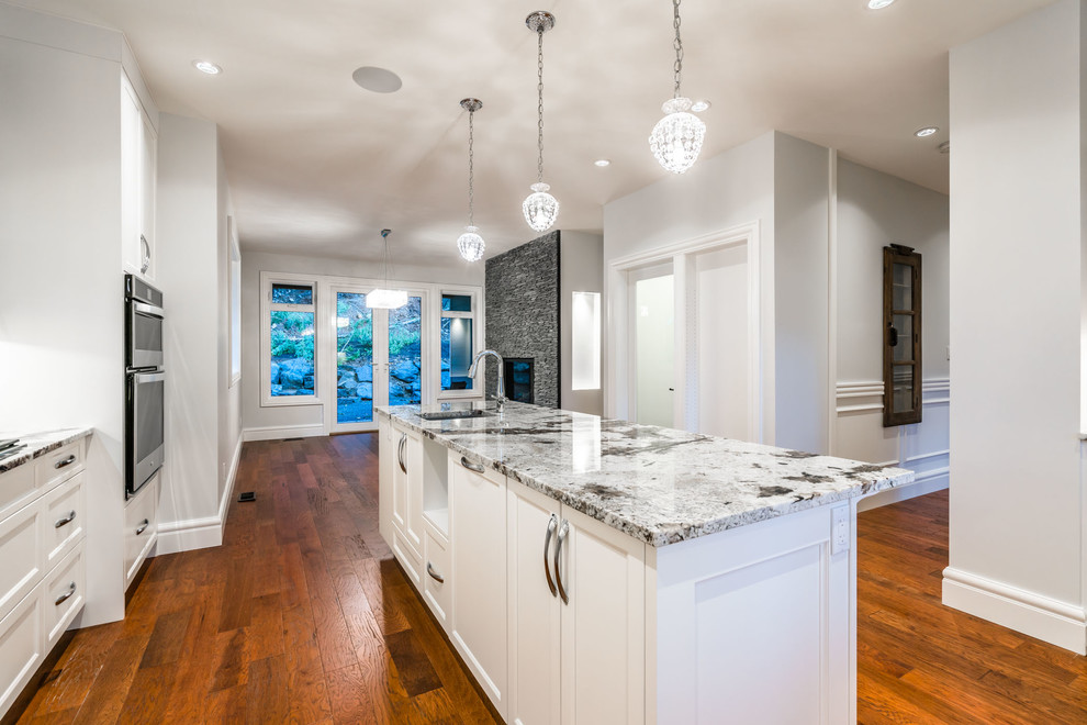 Large transitional u-shaped dark wood floor and brown floor eat-in kitchen photo with an undermount sink, recessed-panel cabinets, white cabinets, granite countertops, white backsplash, ceramic backsplash, stainless steel appliances, an island and multicolored countertops