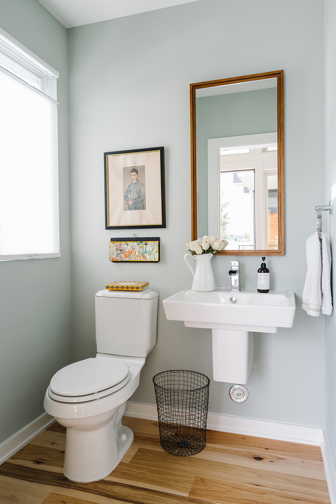 Design ideas for a mid-sized scandinavian powder room in Austin with light hardwood floors, a wall-mount sink and a one-piece toilet.