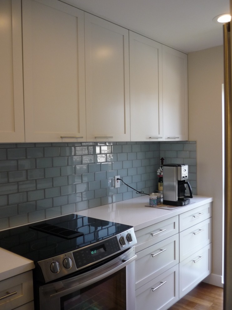 Photo of a small beach style u-shaped separate kitchen in Los Angeles with shaker cabinets, yellow cabinets, quartz benchtops, blue splashback, glass tile splashback, stainless steel appliances and light hardwood floors.