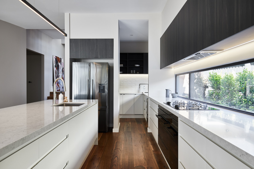 Foto på ett stort funkis kök, med en undermonterad diskho, fönster som stänkskydd, rostfria vitvaror, mellanmörkt trägolv, en köksö och brunt golv