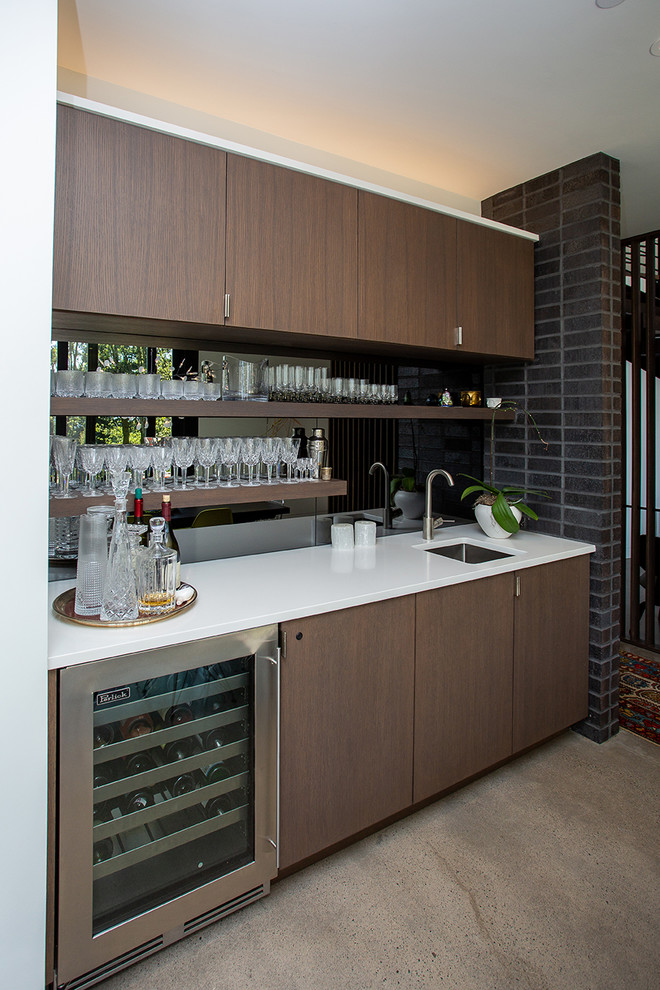 Midcentury single-wall wet bar in Portland with an undermount sink, flat-panel cabinets, dark wood cabinets, mirror splashback, grey floor, white benchtop and concrete floors.