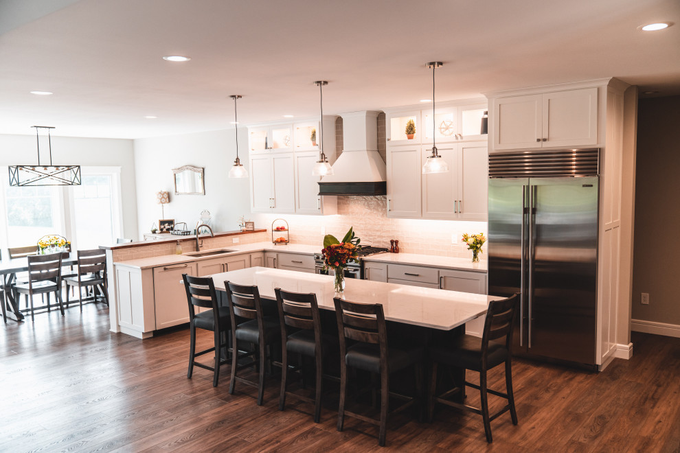 Kitchen pantry - large transitional l-shaped vinyl floor and brown floor kitchen pantry idea with an undermount sink, shaker cabinets, white cabinets, quartz countertops, gray backsplash, subway tile backsplash, stainless steel appliances, an island and white countertops