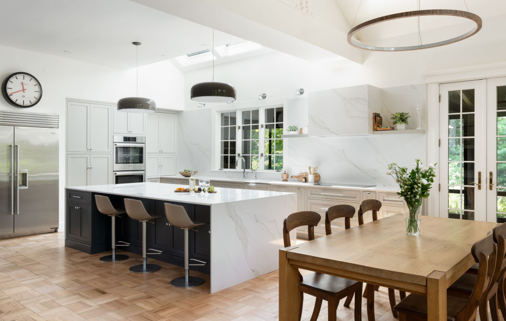 Large transitional light wood floor eat-in kitchen photo with an undermount sink, recessed-panel cabinets, gray cabinets, quartz countertops, white backsplash, quartz backsplash, stainless steel appliances, an island and white countertops